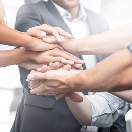 9 Kollegen im Kreis legen die Hände übereinander, Teamwork