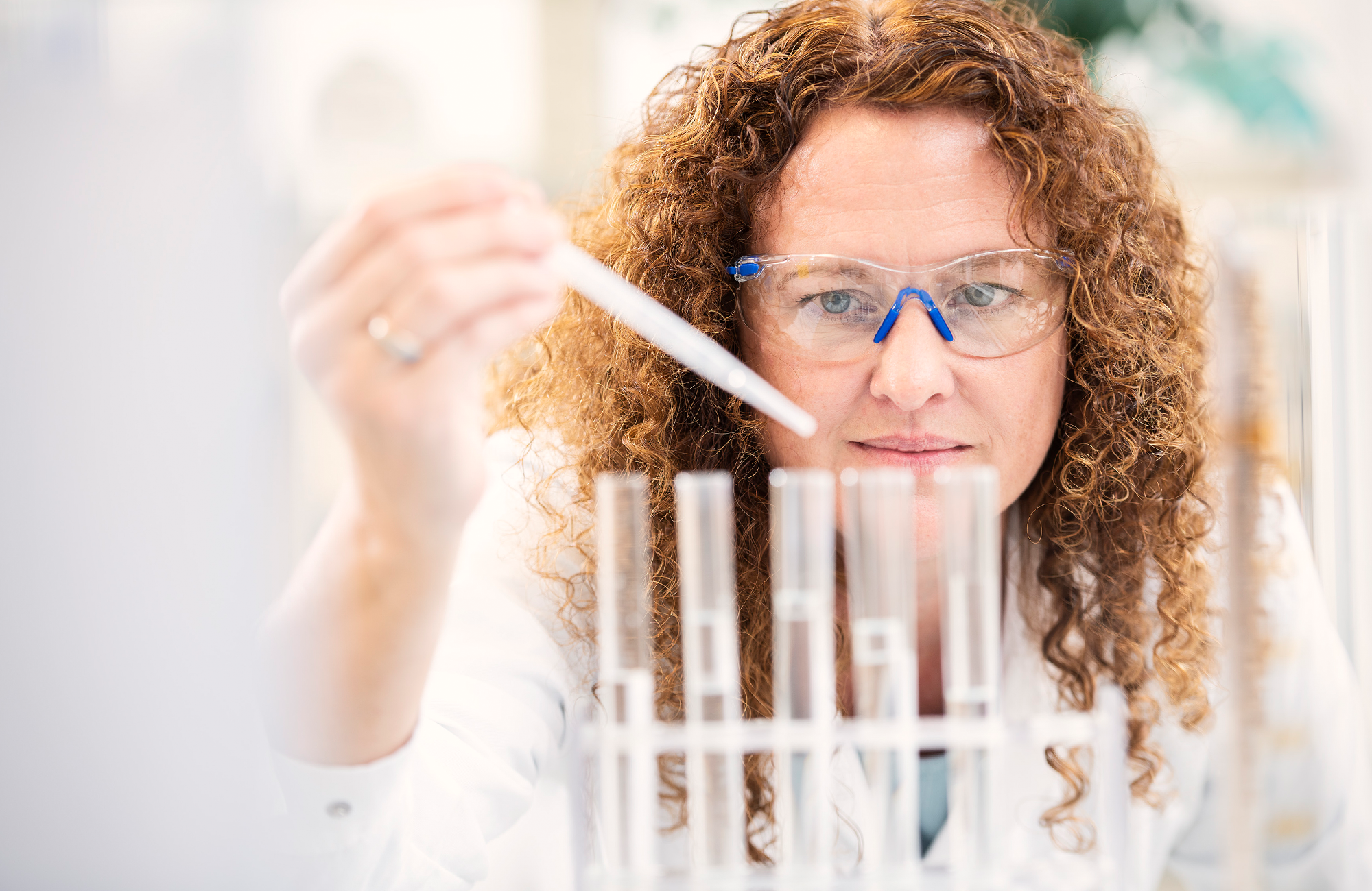 Bioselect Diagnostik Frau mit Pipette Schutzbrille und Reagenzgläsern