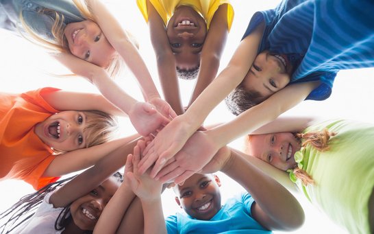 Grundschüler halten Hände zusammen - Symbol für Zusammenhalt