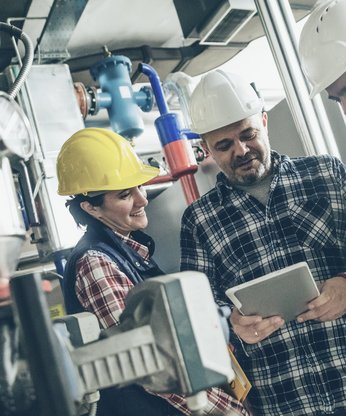 Mitarbeiter in der Produktionsanlage schauen auf ein iPad