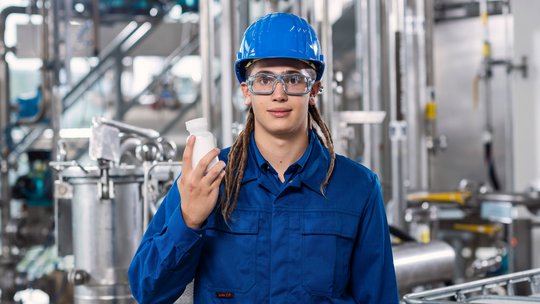 Chemikant in der Produktionsanlage mit Produkt in der rechten Hand