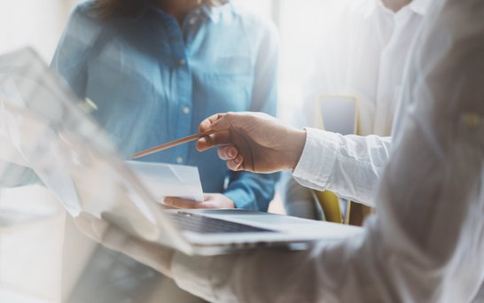 ein Person zeigt mit dem Stift auf ein Mac-Book