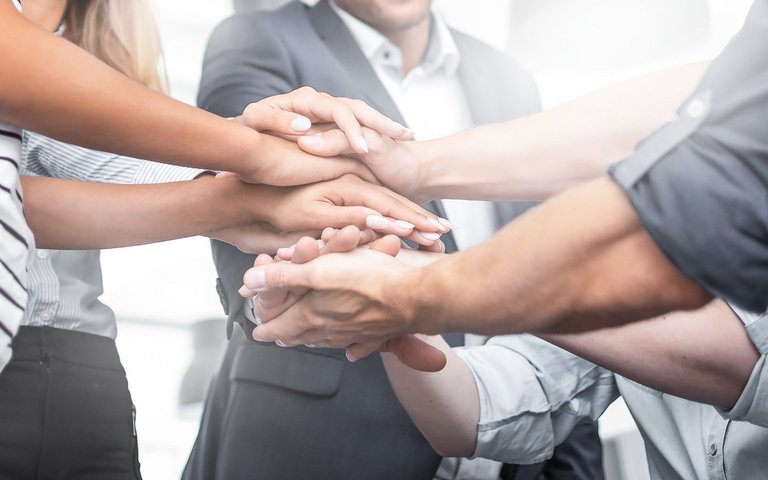 9 Kollegen im Kreis legen die Hände übereinander, Teamwork